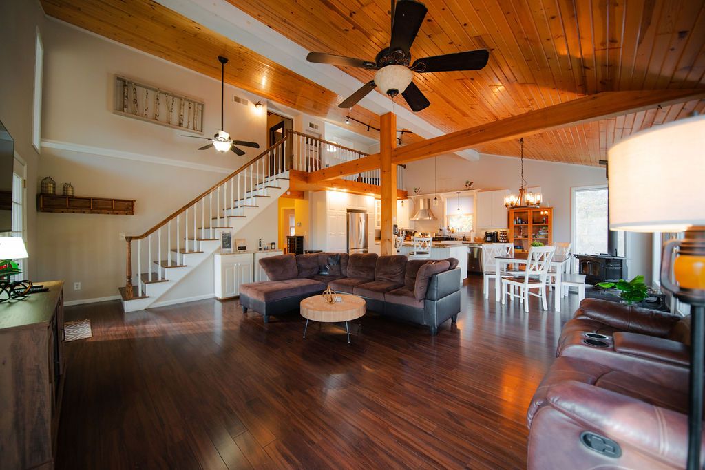 A spacious living room with a wooden ceiling, a large sectional sofa, a round coffee table, and a staircase leading to an upper level.
