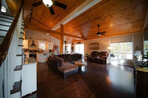 A spacious living area with a wooden ceiling, a kitchen in the background, and a staircase on the left.