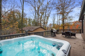 Un jacuzzi en una terraza con vista a árboles y una casa al fondo.
