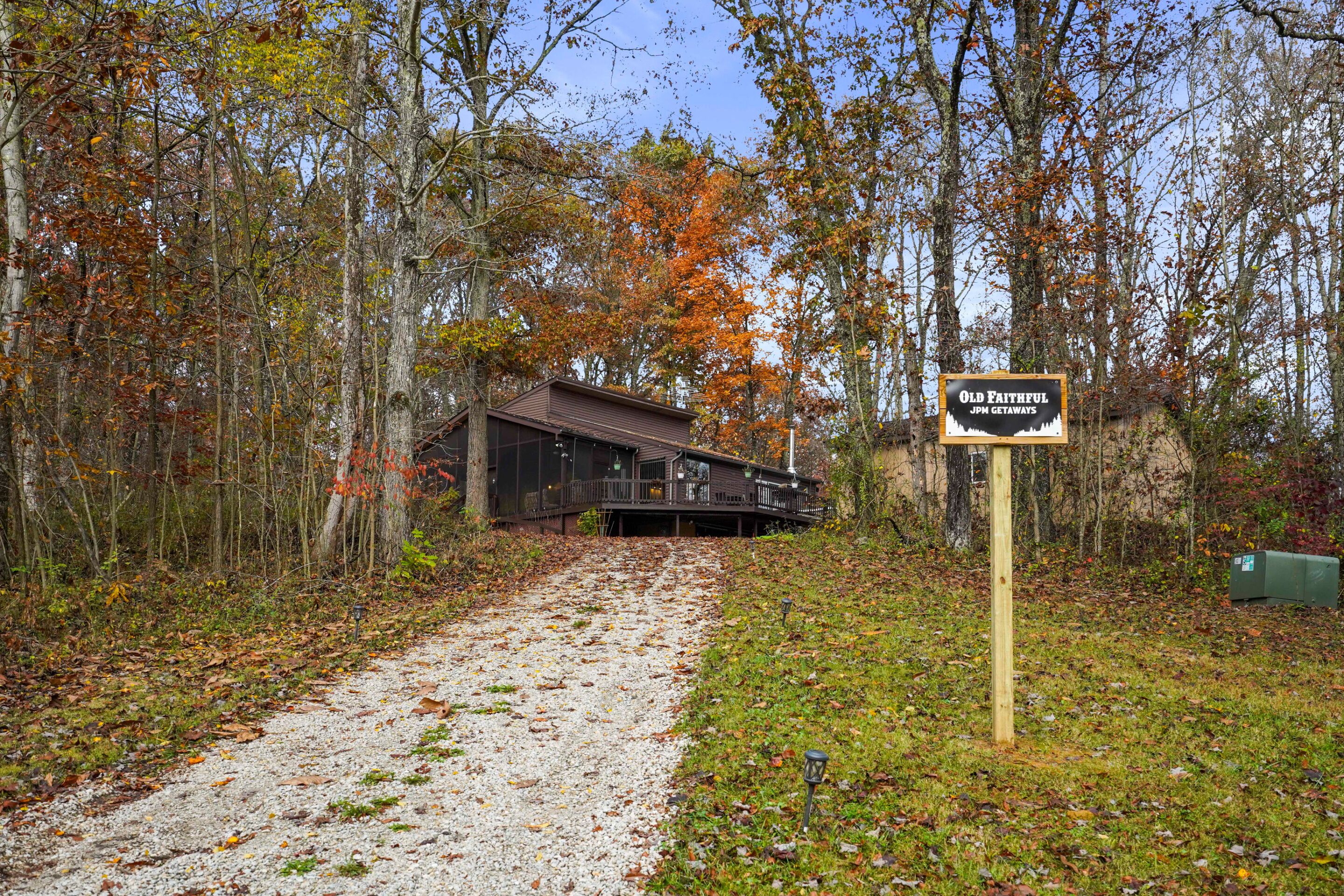 Ein Kiesweg führt zu einer Hütte mit der Aufschrift 'Old Faithful JPM Getaways', umgeben von Herbstlaub.