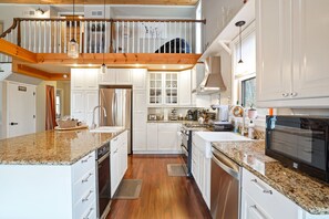 A spacious kitchen with granite countertops, white cabinetry, and a wooden floor.