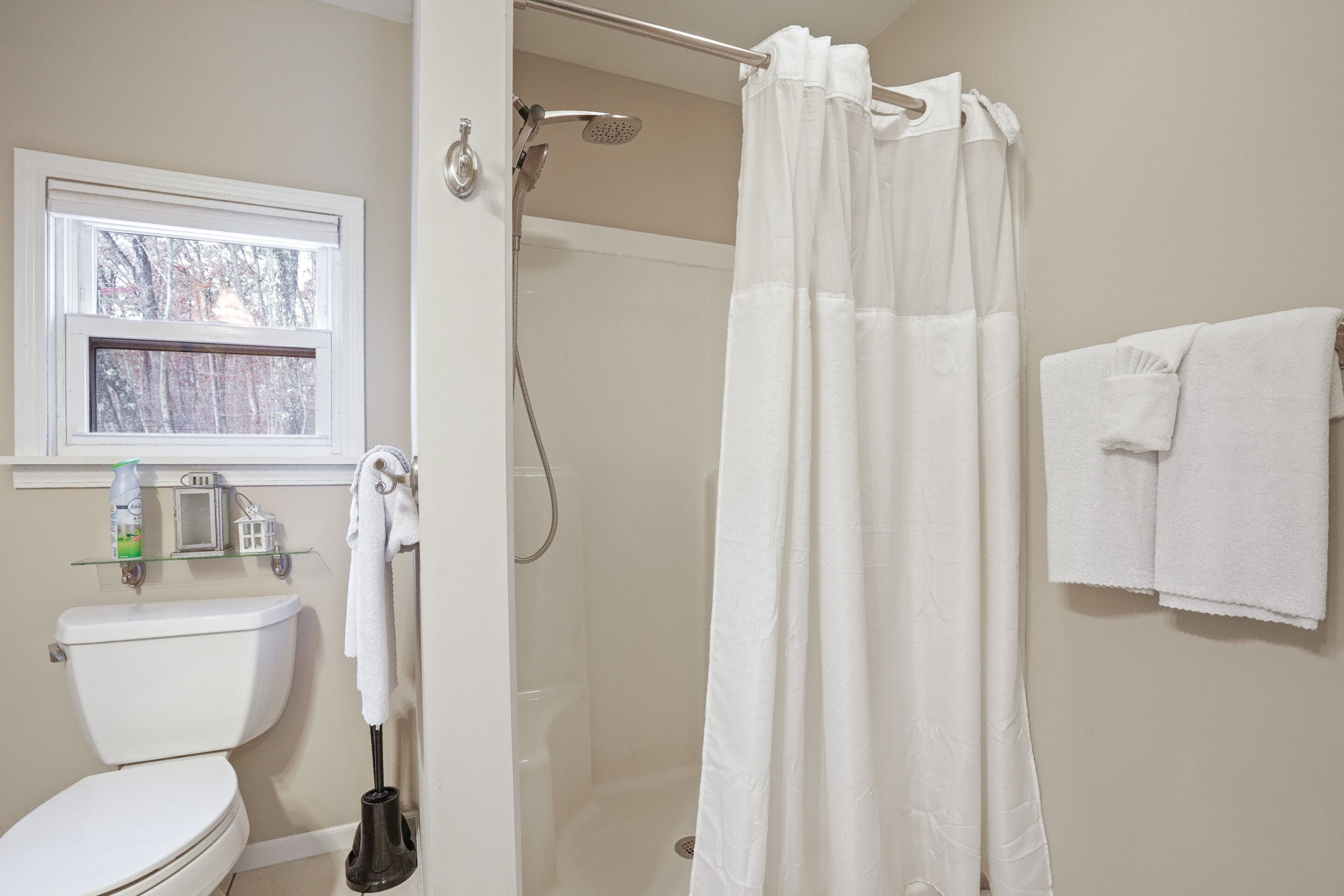 Ein Badezimmer mit Toilette, Dusche, einem Fenster und einem Handtuchhalter.