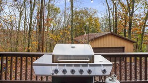 A barbecue grill with four burners, a control panel, and a gas tank.