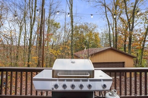 A barbecue grill on a deck with a view of trees and a shed in the background.