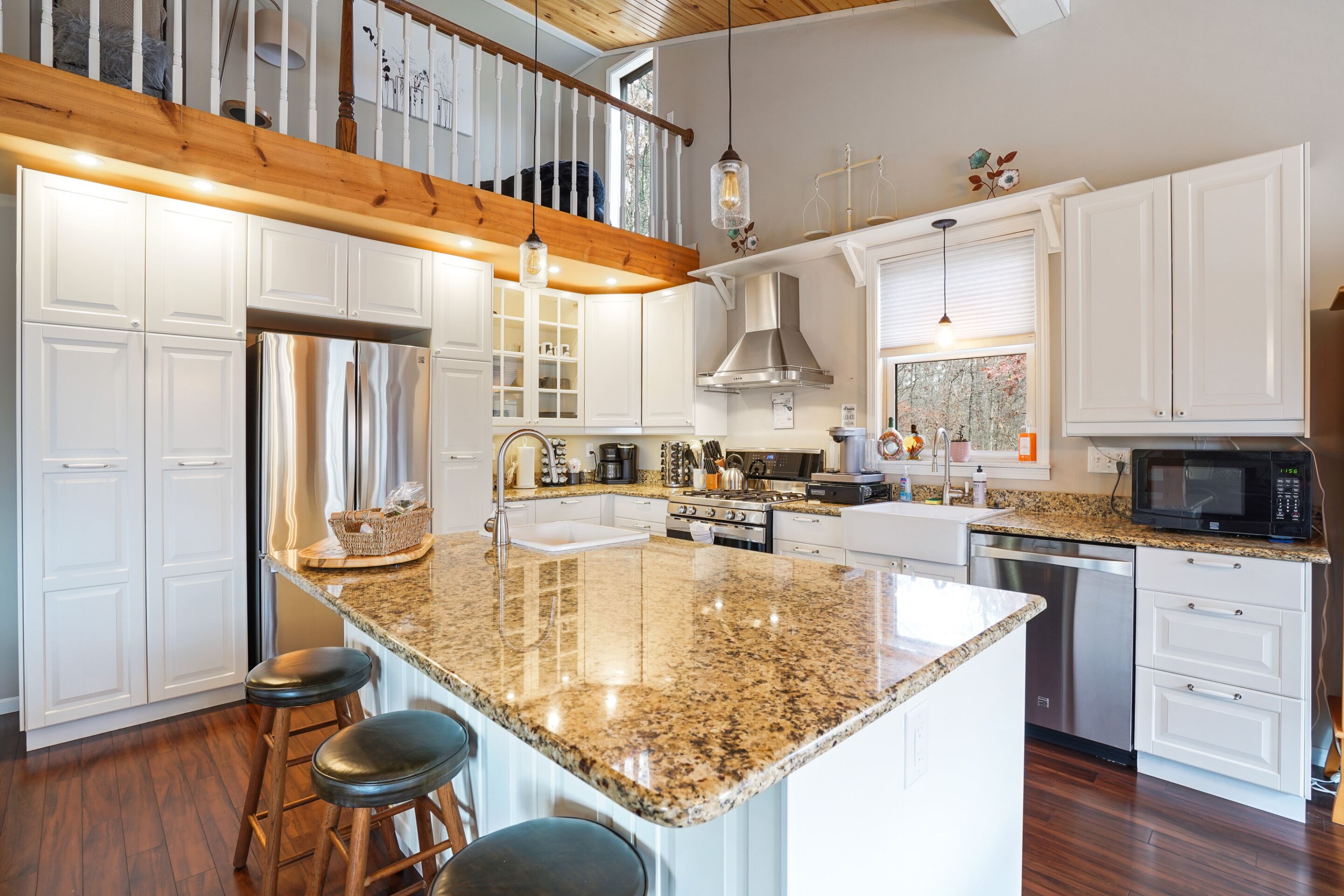 A modern kitchen with white cabinetry, granite countertops, stainless steel appliances, and a wooden staircase.