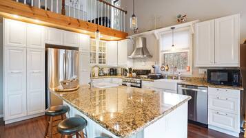 A modern kitchen with white cabinetry, granite countertops, stainless steel appliances, and a wooden staircase.