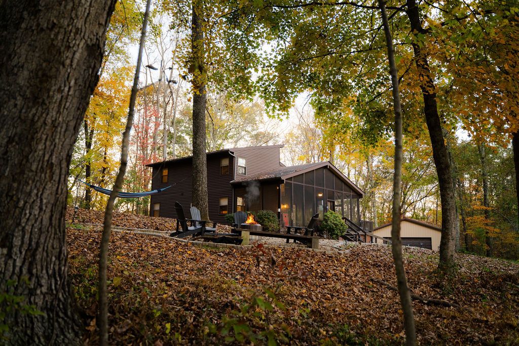 A cabin with a deck, surrounded by trees and autumn leaves.