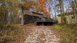 A cabin with a deck and a covered walkway, surrounded by trees with autumn foliage.