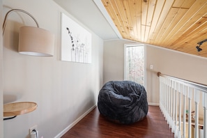 A modern interior with a wooden ceiling, a bean bag chair, a wall-mounted lamp, and a framed artwork.