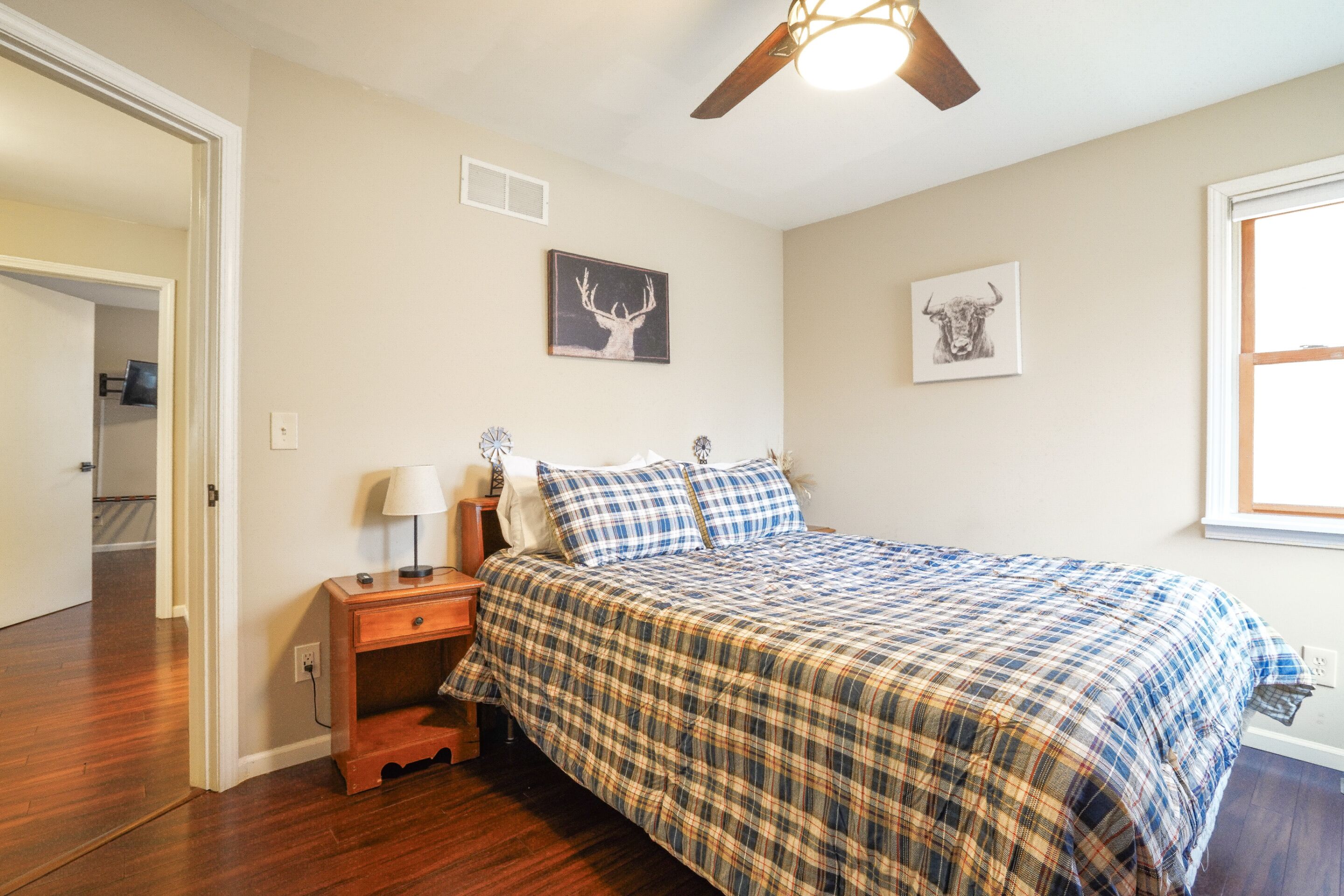 A bedroom with a bed, a nightstand, a ceiling fan, and two wall-mounted pictures.