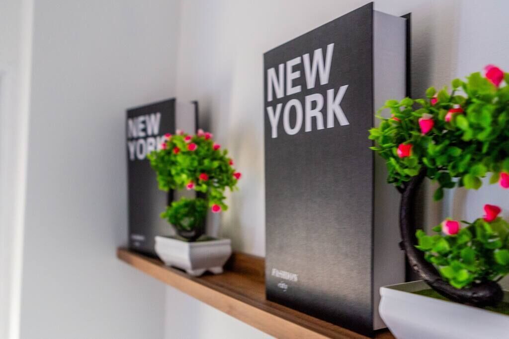 Un muro con due pannelli neri recanti la scritta 'NEW YORK' e una pianta in vaso con fiori rosa.