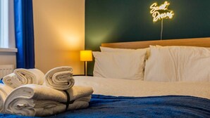 Una cama bien hecha con sábanas blancas, una manta azul y un letrero de neón en la pared que dice 'Sweet Dreams'.