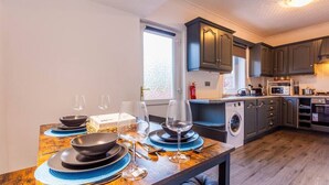 Una cocina compacta con armarios oscuros, lavadora y comedor con platos, tazones y copas de vino.