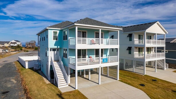 A two-story beachfront house with a balcony, a covered porch, and a staircase leading to the upper level. - Ocean Breeze: Dog-Friendly w/Views, Elevator, Private Pool, Large fenced in Yard (Kitty Hawk)