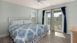 Un dormitorio con cama, ventilador de techo, ventana con cortinas y vista a un balcón.
