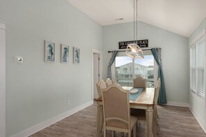 A dining area with a table and chairs, a hanging light fixture, and a sign above the window. - Ocean Breeze: Dog-Friendly w/Views, Elevator, Private Pool, Large fenced in Yard (Kitty Hawk)