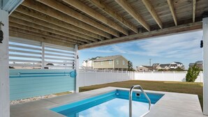 A covered outdoor swimming pool with a wooden ceiling and a view of houses in the background. - Ocean Breeze: Dog-Friendly w/Views, Elevator, Private Pool, Large fenced in Yard (Kitty Hawk)