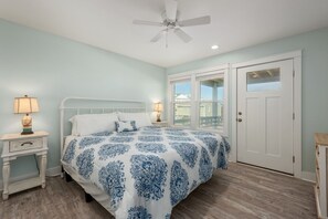 A bedroom with a bed, two bedside tables, a ceiling fan, and a door. - Ocean Breeze: Dog-Friendly w/Views, Elevator, Private Pool, Large fenced in Yard (Kitty Hawk)