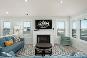 Un salon avec une cheminée, un canapé bleu, une table basse et un téléviseur diffusant une émission sur les « Vacances et promotions à Coastal Carolina ».