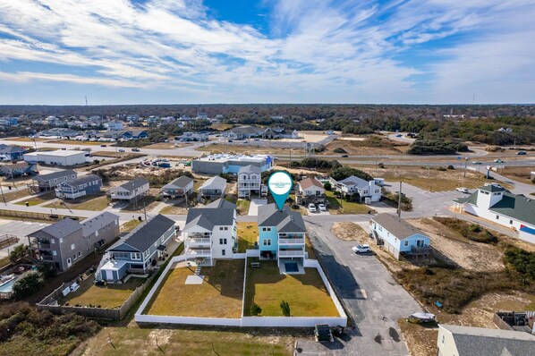 An aerial view of a residential area with houses, a central building with a balcony, and a clear sky.