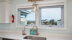 A kitchen with a large window, a hanging light fixture, and a fire extinguisher. - Ocean Breeze: Dog-Friendly w/Views, Elevator, Private Pool, Large fenced in Yard (Kitty Hawk)
