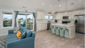 A modern kitchen with white cabinets, a central island with bar stools, and a large refrigerator. - Ocean Breeze: Dog-Friendly w/Views, Elevator, Private Pool, Large fenced in Yard (Kitty Hawk)
