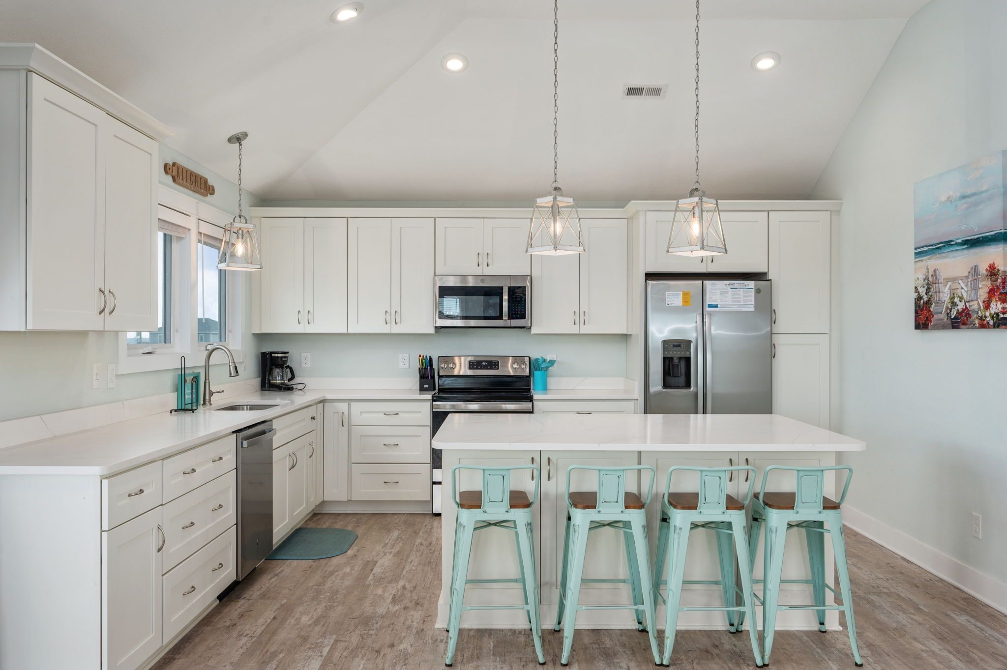 A modern kitchen with white cabinets, stainless steel appliances, and teal bar stools.