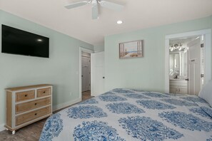A bedroom with a bed, dresser, TV, and a door leading to a bathroom.