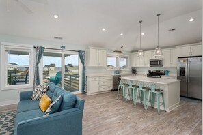 A modern kitchen with white cabinets, a central island with bar stools, and a view to the outside.