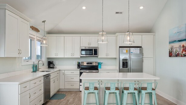 A modern kitchen with white cabinets, stainless steel appliances, and a central island with bar stools. - Ocean Breeze: Dog-Friendly w/Views, Elevator, Private Pool, Large fenced in Yard (Kitty Hawk)