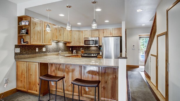 A modern kitchen with wooden cabinets, a granite countertop, stainless steel appliances, and pendant lighting. - Ten Mile Townhouse in Downtown Frisco | Riverside! (Frisco)