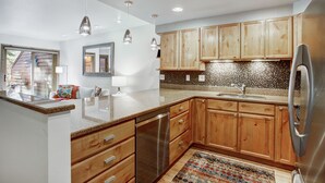 A modern kitchen with wooden cabinets, a stainless steel refrigerator, and a tiled backsplash. - Ten Mile Townhouse in Downtown Frisco | Riverside! (Frisco)