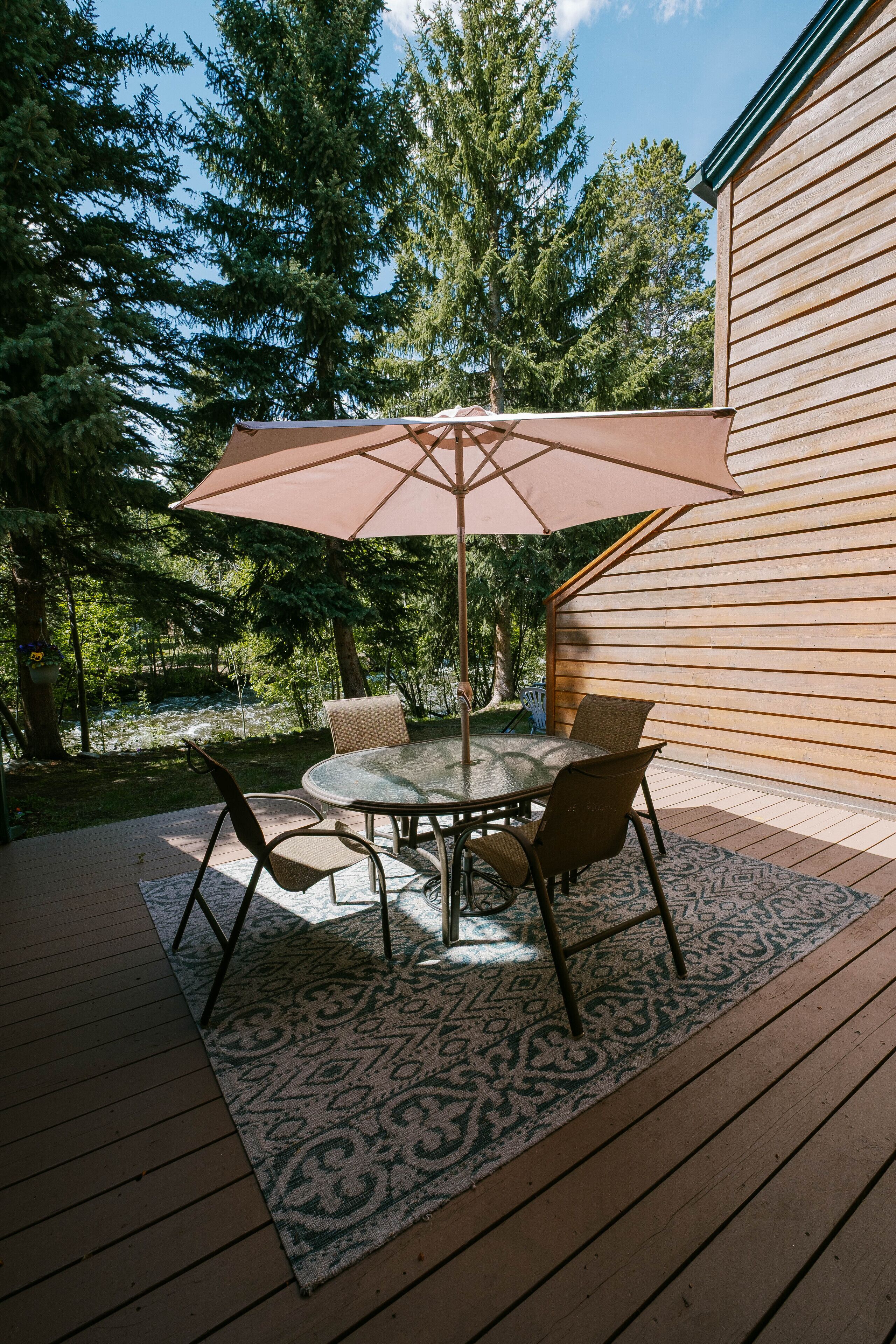 Um pátio externo com uma mesa redonda e cadeiras, um grande guarda-sol e um deck de madeira.