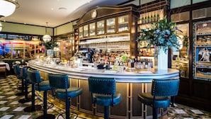 Una zona de bar con un mostrador curvo, taburetes, un reloj y un gran arreglo floral.
