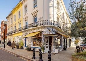 Un immeuble d’angle avec un commerce au rez-de-chaussée, un balcon orné de balustrades décoratives et une enseigne indiquant « Clarendon Cross ».