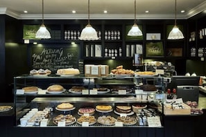 Une vitrine de boulangerie présentant diverses pâtisseries et gâteaux, un menu écrit à la craie et des lampes suspendues.