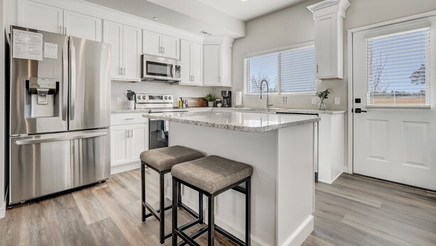 A modern kitchen with white cabinetry, stainless steel appliances, and a central island with stools. - Rising Star (Colorado Springs)