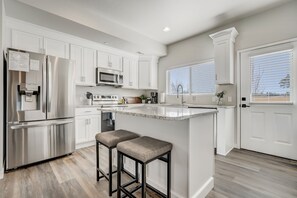 Une cuisine moderne avec des meubles blancs, des appareils en acier inoxydable et un îlot central doté de tabourets.