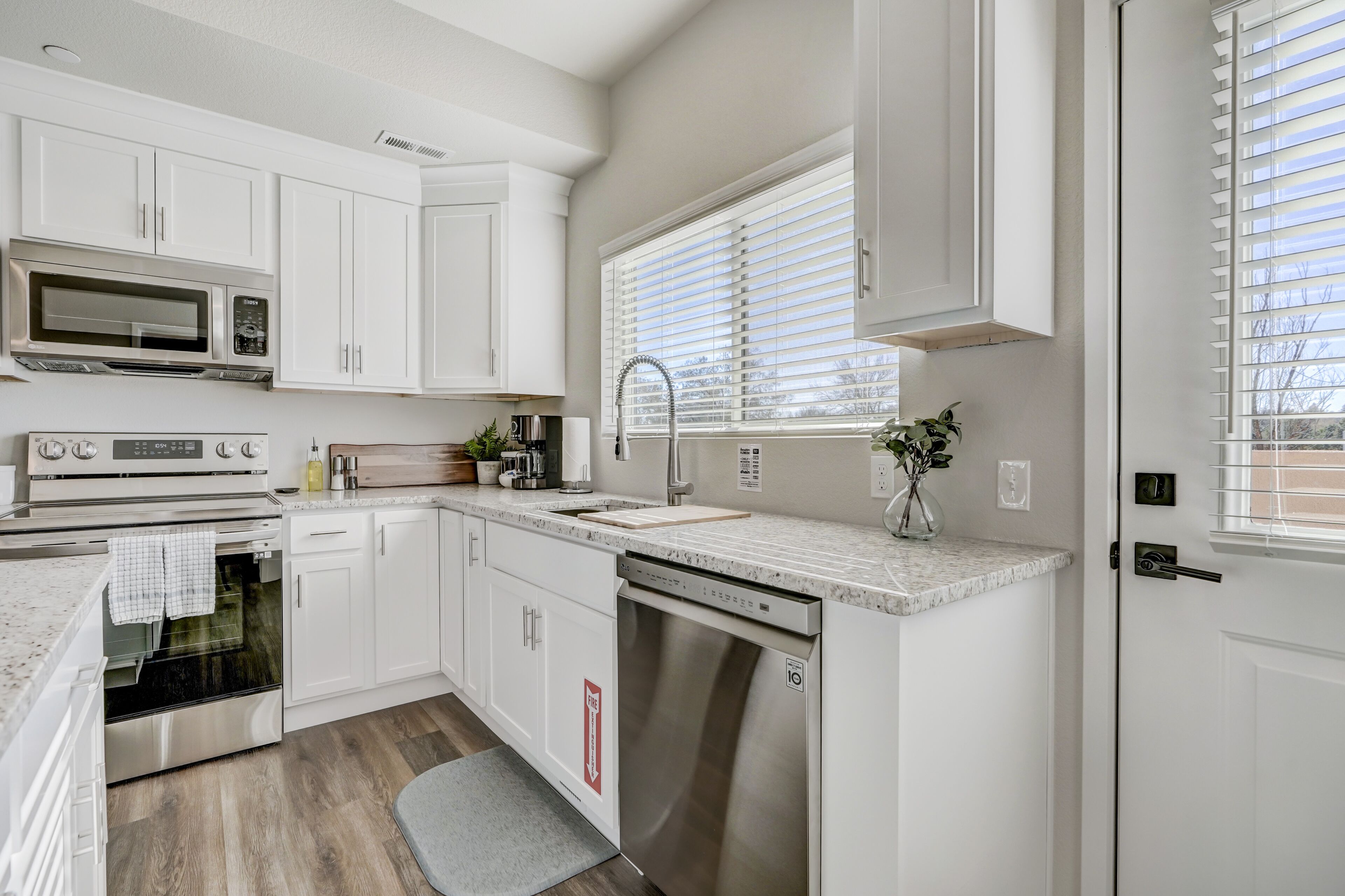 A modern kitchen with white cabinetry, stainless steel appliances, a built-in dishwasher, and a window with blinds.