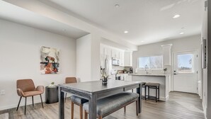 A modern kitchen with white cabinets, a dining area with a dark wood table and chairs, and a large window providing natural light. - Rising Star (Colorado Springs)