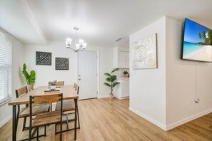 A modern dining area with a wooden table and chairs, a chandelier, and a potted plant.