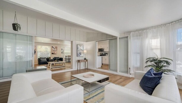 A modern living room with white furniture, a glass coffee table, and a view into the kitchen. - Spacious home With Heated Pool 3 miles from IMG! (Bradenton)
