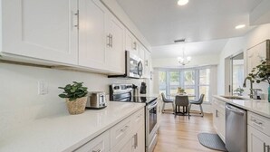 A modern kitchen with white cabinets, stainless steel appliances, and a dining area with a table and chairs. - Spacious home With Heated Pool 3 miles from IMG! (Bradenton)