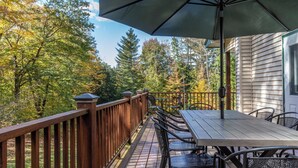 Eine Holzterrasse mit Tisch und Stühlen, umgeben von Bäumen und einem Haus.