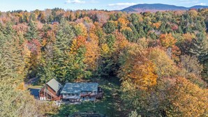 Eine Hütte mit einer großen Terrasse und einer Garage, umgeben von dichtem Wald mit Herbstlaub.