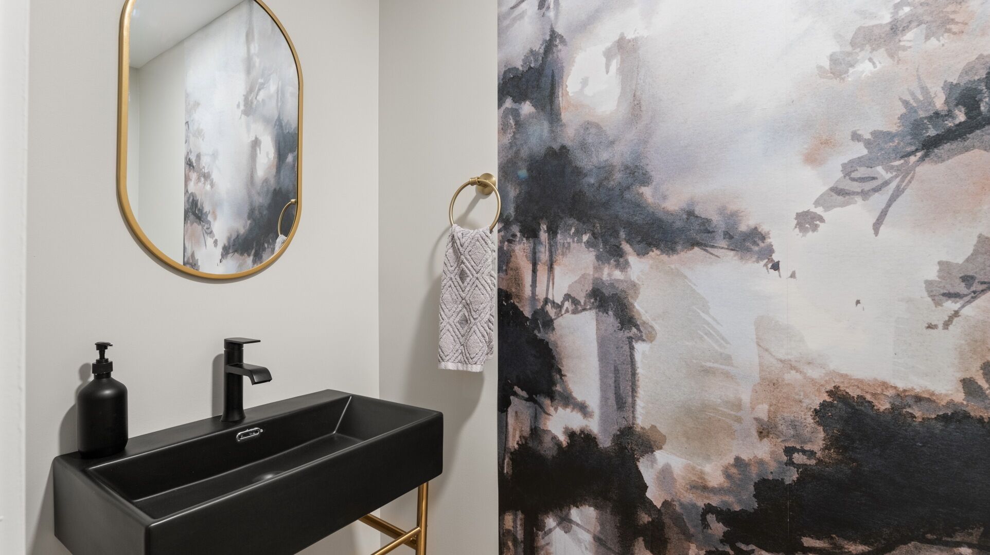 A bathroom with a black sink, a gold-framed mirror, and a towel hanging on a towel ring.