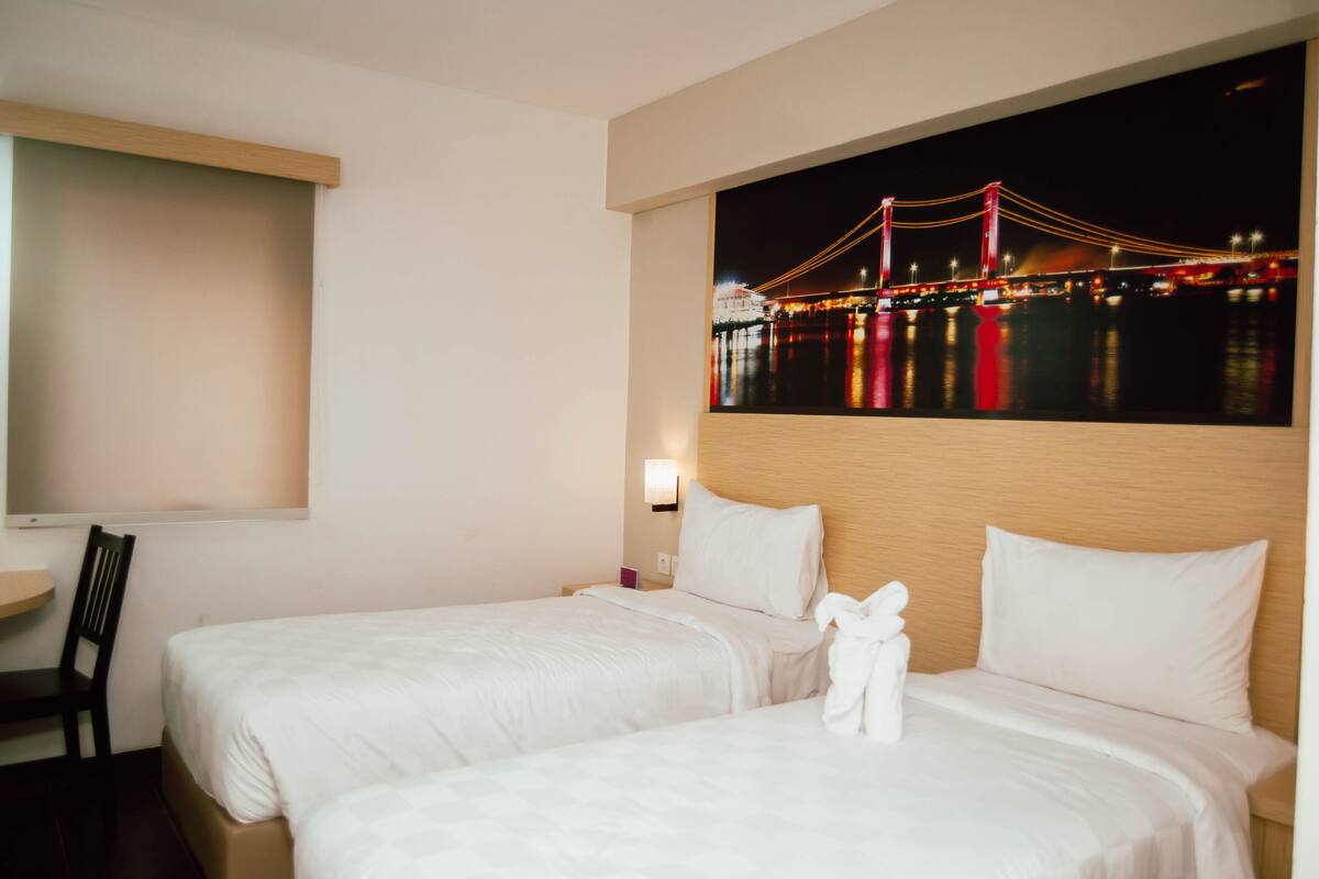 Une chambre d’hôtel avec deux lits, une table de chevet, une chaise et un téléviseur fixé au mur.