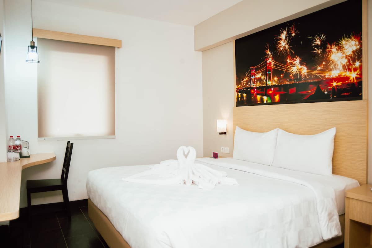 Une chambre d’hôtel avec un lit, un bureau, une chaise et un tableau représentant des feux d’artifice accroché au mur.