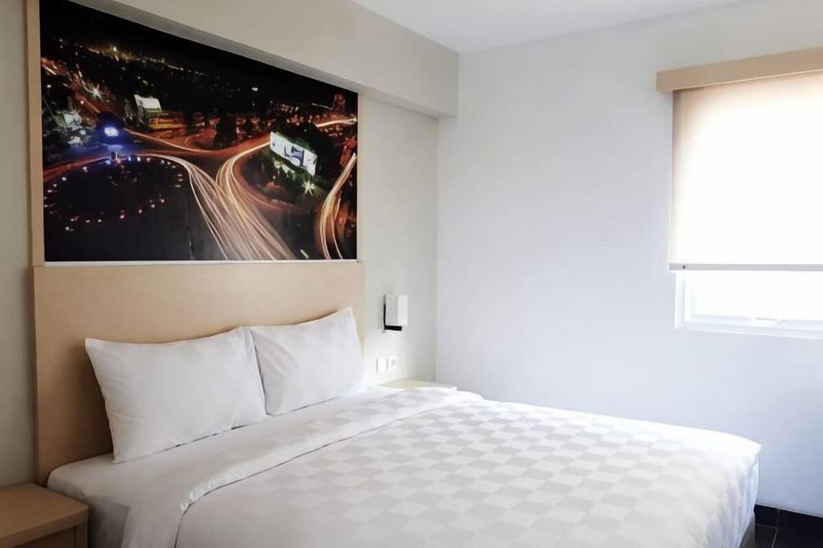 Une chambre d’hôtel avec un lit, un tableau représentant une vue nocturne, une fenêtre et une table de chevet.