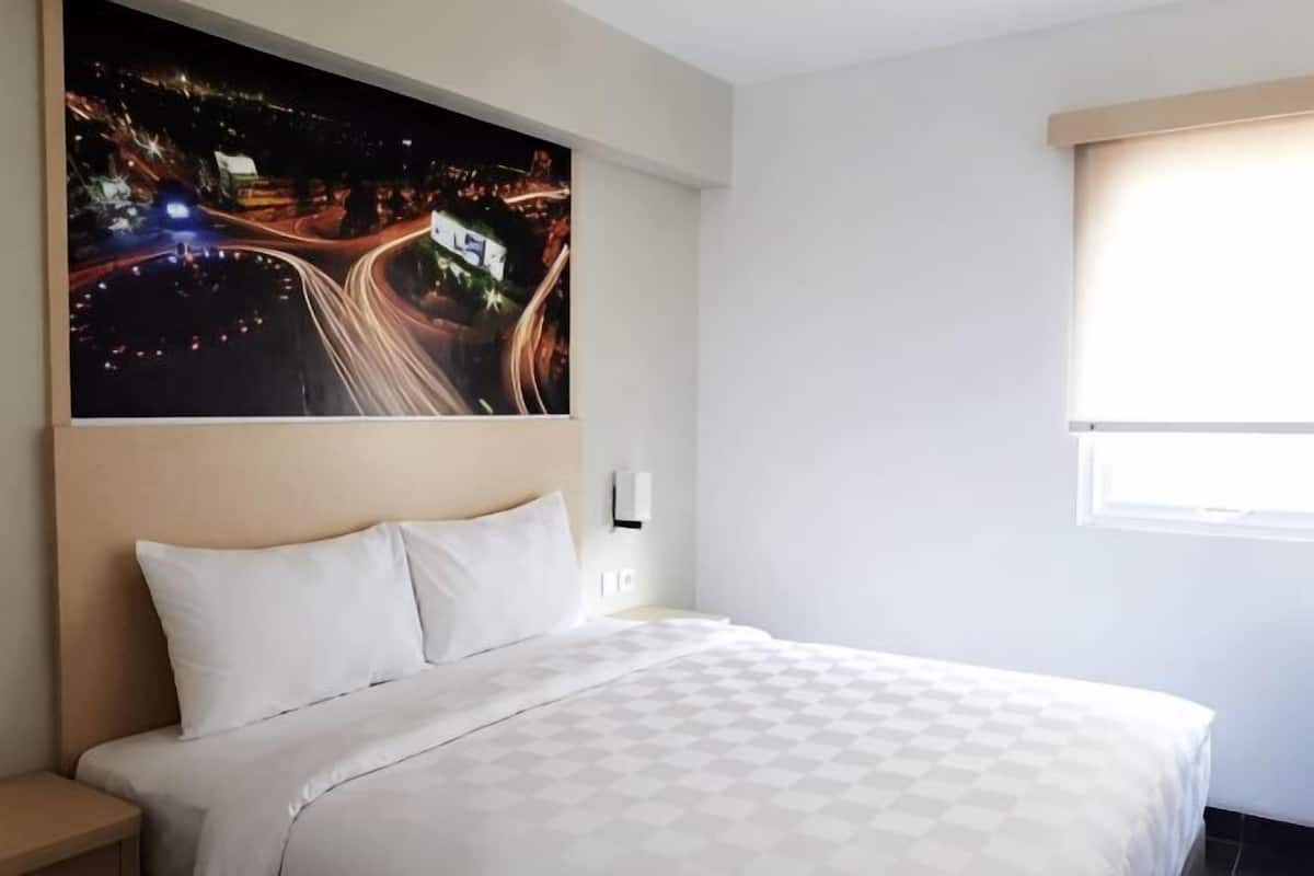 A hotel room with a bed, a night view painting, a window with blinds, and a nightstand.